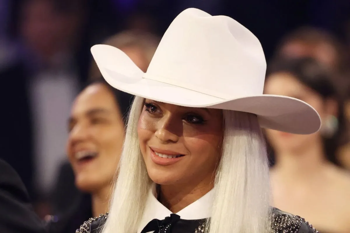 Beyoncé souriante coiffée d'un grand chapeau de cowboy blanc lors d'un événement.