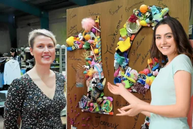 Femme souriante à côté d'un panneau en forme de cœur décoré d'objets recyclés lors d'un événement de mode.