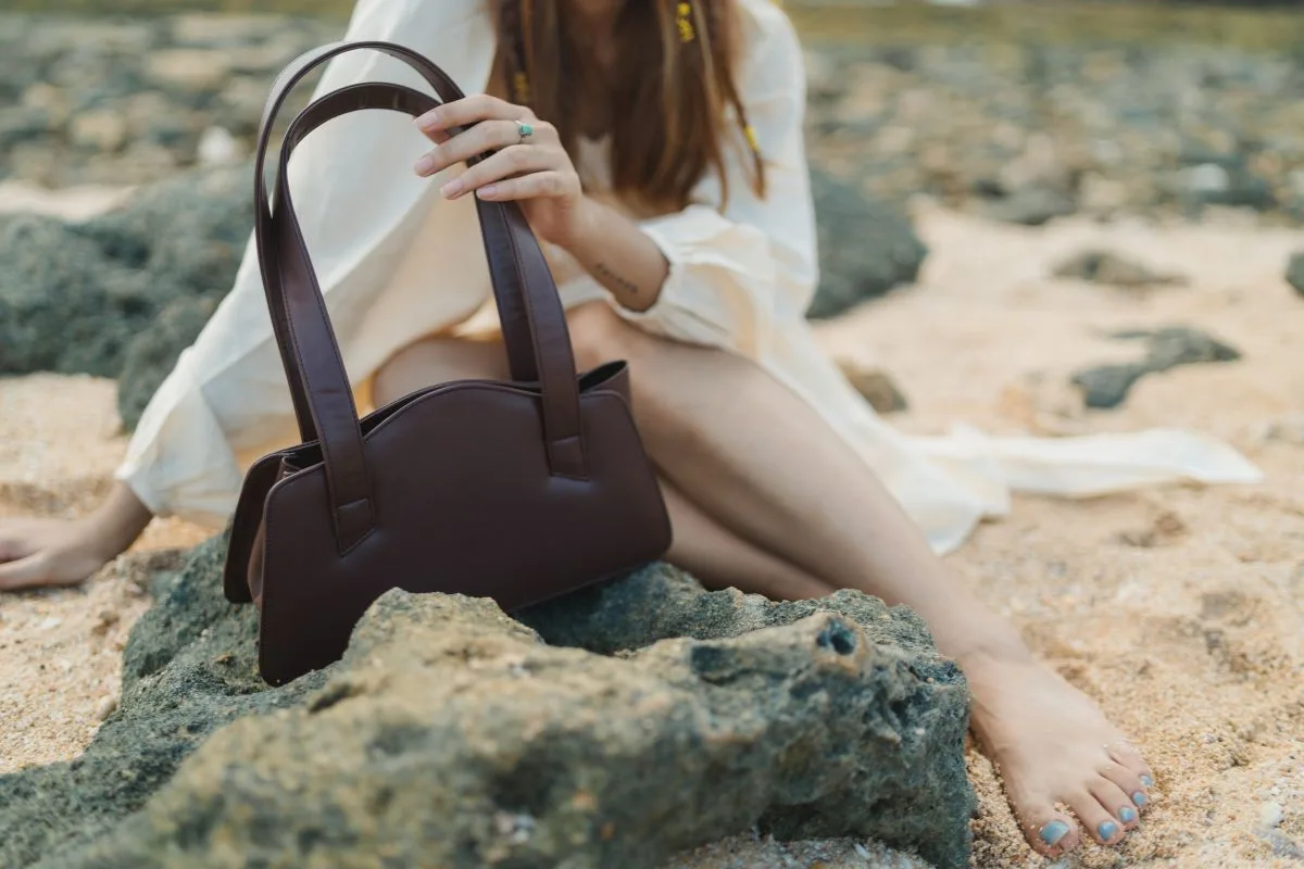 Sac en cuir vegan tenu par une femme assise sur une plage.