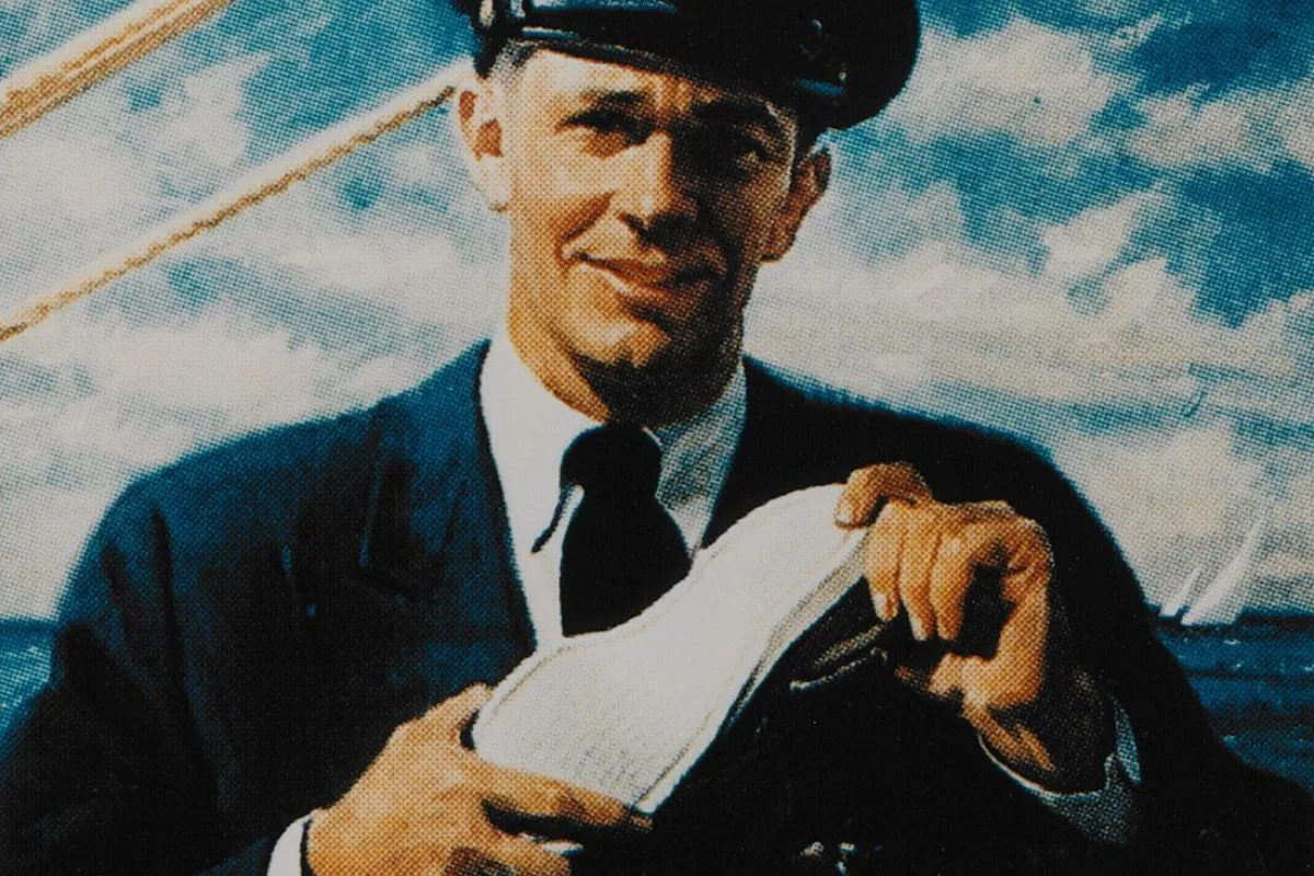 Portrait de Paul Sperry tenant une chaussure bateau devant un décor marin.