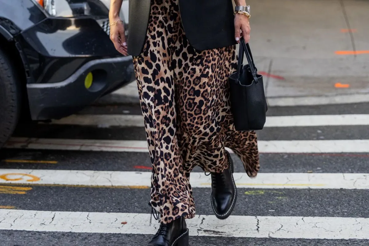Photo de femme traversant la rue, vêtue d'un pantalon à imprimé léopard et de bottes noires.