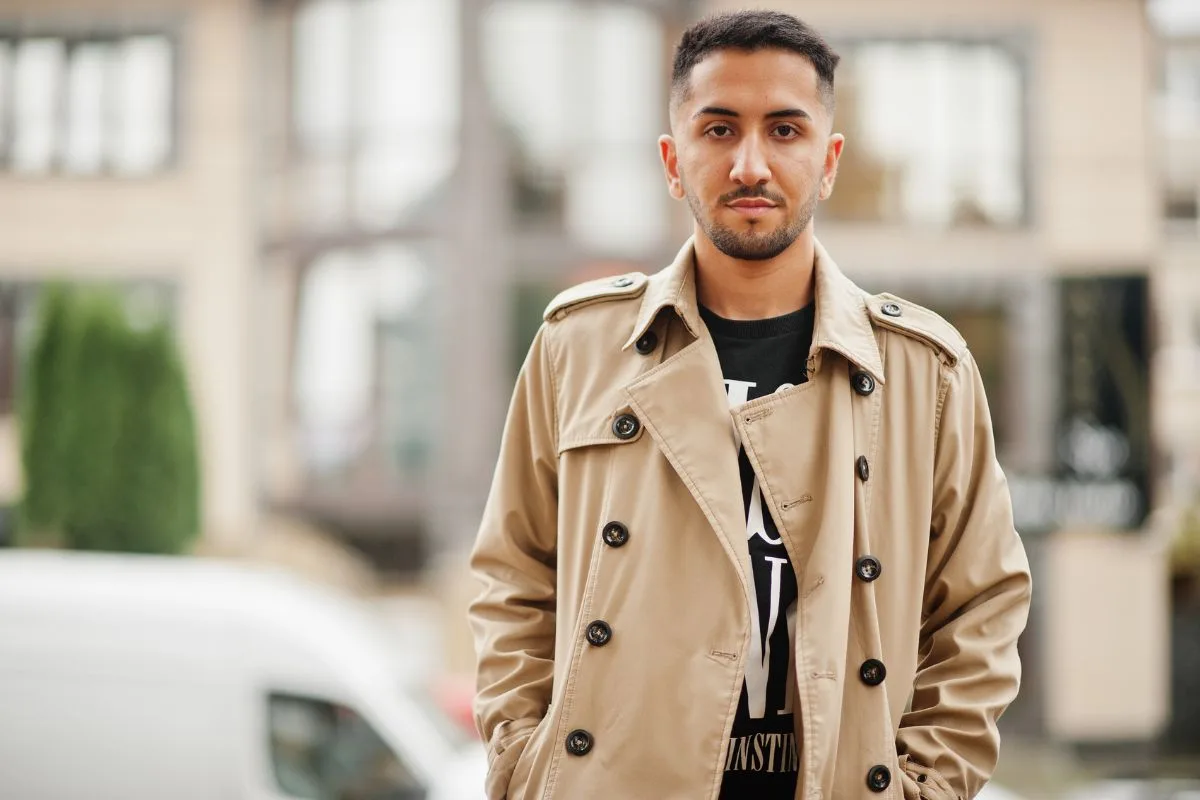 Homme portant un trench-coat beige classique sur un t-shirt graphique, incarnant l'élégance décontractée du printemps.