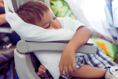 Endormir les enfants durant un vol : Un enfant dort paisiblement dans son siège d'avion, appuyé sur un coussin blanc.